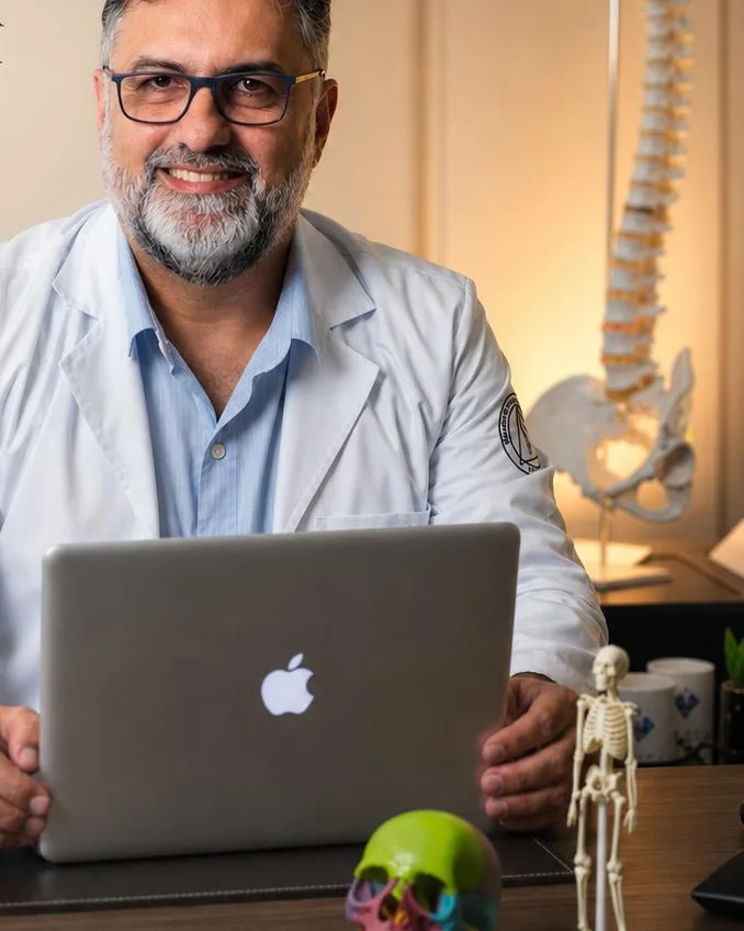 Dr. Jorge Costa, fisioterapeuta osteopata, no consultório em Macaé, ao lado de um modelo de coluna vertebral